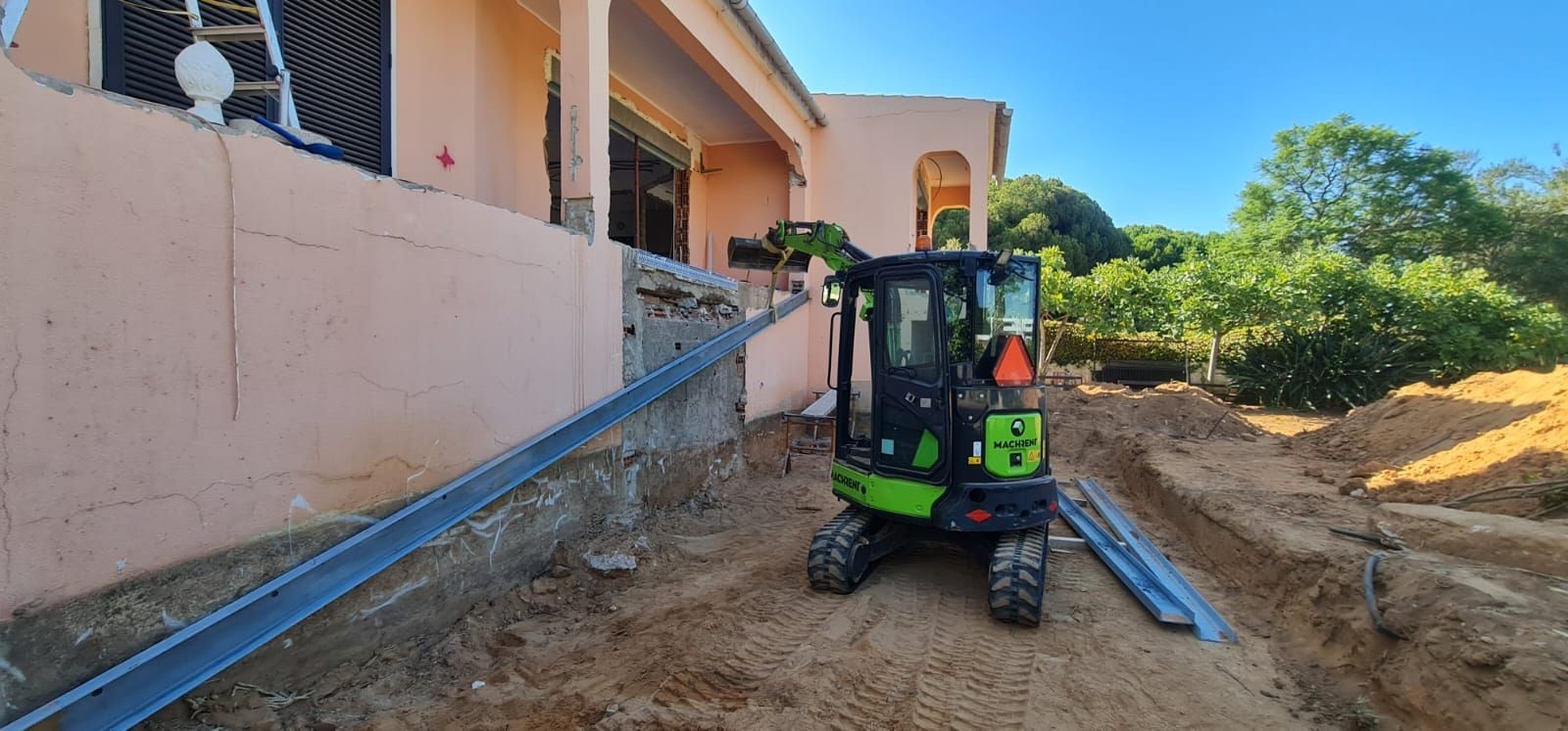 Mini excavator at a construction site beside a partially demolished building.